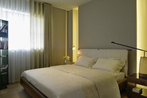 White double bed with upholstered headboard against grey wall in modern bedroom with two tall, narrow widows and one large window