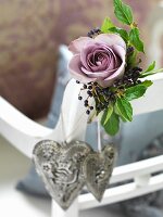 Small arrangement with dusky pink rose and grey love-heart pendants on backrest of white chair