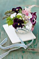 Spring posy of pansies, violas, astilbes, lilac, flowering currant and apple blossom with ribbon on white tile