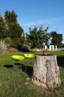 Tree trunk used as garden table and two neon yellow bar stools in summer garden