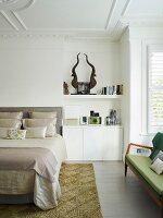 Teilweise sichtbares, elegantes Doppelbett mit drapierten Kissen, neben in Nische eingebaute Unterschränke in Weiß, auf Ablage stilisierte Trophäe, in traditionellem Schlafzimmer