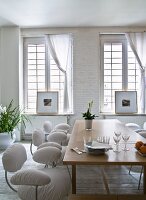 Gepolsterte Stühle mit weißem Überzug um Holztisch vor Sprossenfenster