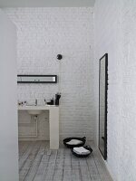 Washstand against whitewashed brick wall and baskets on towels on wooden floor in ensuite bathroom