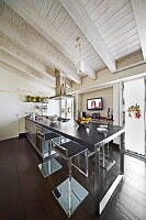 Modern kitchen counter with dark worksurface on metal frame and bar stools in rustic interior with white-painted wooden ceiling
