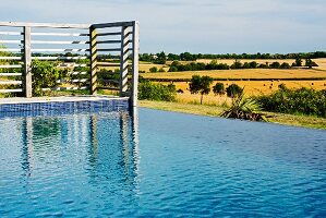 Infinity pool with slatted wooden wall on terrace in Mediterranean landscape