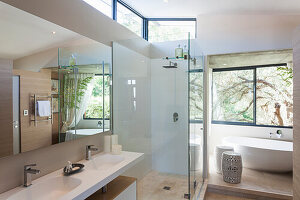 Modern bathroom with glass shower and free-standing bathtub, view of the trees outside