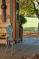 Old wooden chair with rustic painted pattern in entrance of wooden house with view of sunny lawn and trees