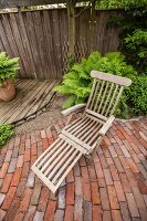 Wooden sun lounger in corner of rustic garden with wooden decking, gravel area and brick-paved terrace