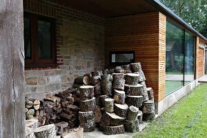 Firewood stacked in façade niche of modern house with wooden cladding and stone walls