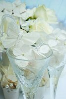 Stemmed glasses decorated with white hydrangea florets and butterfly ornaments in front of hydrangea plant