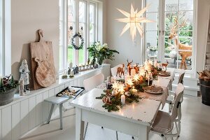 Christmas table decorated with fir branches and illuminated stars in front of French windows with view of fake reindeer