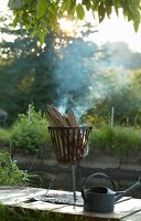 Feuerkorb mit brennenden Holzscheiten und Vintage Zinkgiesskanne im Freien