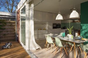 Blick von Terrasse auf Essbereich mit mintfarbenen Klassikerstühlen und weisser Einbauküche
