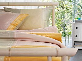 Bamboo bed and yellow bed linen in front of glass wall
