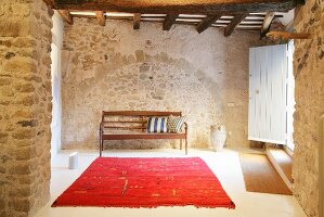 Red rug and wooden bench in foyer of restored stone house