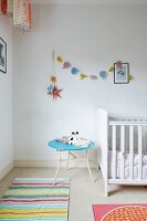 White cot, pale blue side table and pastel garland of elephants in nursery