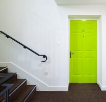 Neon-green panelled door in white stairwell with brown carpet