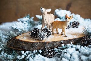 Christmas arrangement of carved deer figurines on slice of log and snowy branches