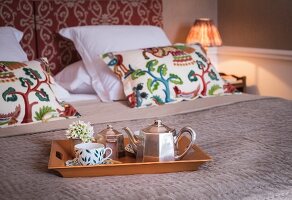 Silver teapot and cup on tray on bed