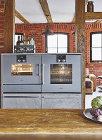 An oven and a steam cooker in a kitchen with a brick wall