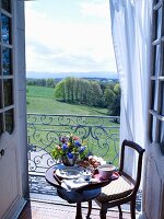 Small table set for breakfast with vase of flowers in front of balcony with a view