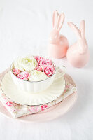 Teacup filled with ranunculus and roses in front of Easter bunnies