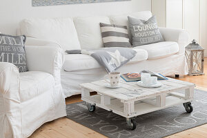 White, loose-covered sofa set and pallet coffee table in living room of converted dairy