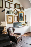 Vintage leather armchair on animal-skin rug, table lamp on steps and various picture frames on wall