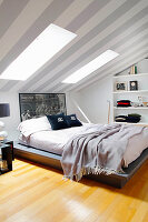 Double bed in attic room with grey and white stripes wallpaper on ceiling