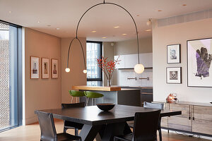 Designer lamps above dining table with open-plan kitchen in background