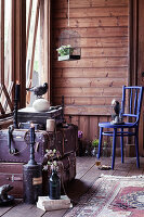 Vintage birdcage, blue chair, stuffed bird and stacked trunks in room with wooden wall