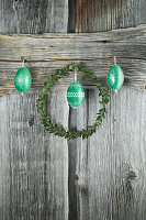 Box wreath and hand-painted green Easter eggs on rustic wooden wall
