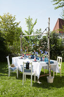Garden table with white tablecloth, blue accents and fairy lights in the summer garden
