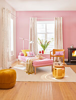 A day bed, a chair, a wood-burner, a golden side table and a pouffe in a living room painted in shades of pink