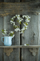 Cherry-blossom heart-shaped wreath on rustic wooden wall and jug of cherry blossoms