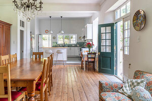 Langer Esstisch aus Holz mit Stühlen in offenem Wohnraum mit Holzdielenboden, im Hintergrund Küche
