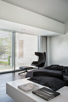 Designer armchair with footstool next to terrace doors in monochrome bedroom
