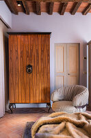 Wardrobe with wood-veneer front next to modern armchair