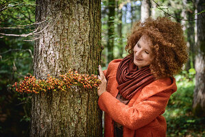 Frau im Wald bindet Girlande aus Hagebutte um einen Baum