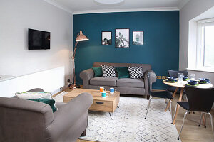 Living room with grey sofa set, dining table and chairs and petrol-blue wall