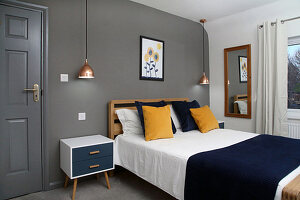 Doppelbett, Nachtkästchen und Pendelleuchten im Schlafzimmer mit dunkelgrauer Wand