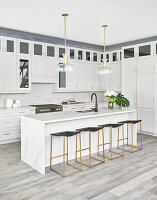 White kitchen with island counter, bar stools and glass and brass pendant lamps