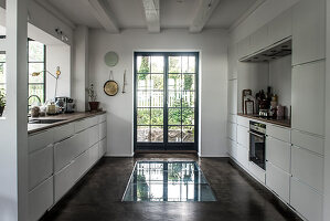 White built-in cabinets in front of window and floor with glass insert in front of French doors in kitchen