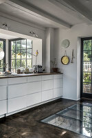 White base cabinets in front of the window and floor with glass insert in the kitchen