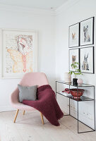 Pink upholstered chair with pillows and blanket, console table, and pictures on the wall