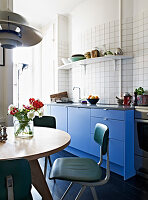 Round table and retro chairs in living room kitchen with blue fronts