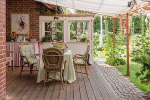 Table and rattan chairs on rustic terrace with awning in garden