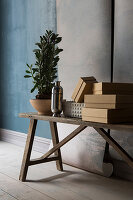 Boxes, vase and plant on wooden bench in front of lengths of wallpaper