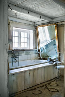 Large gilt-framed mirror above bathtub in rustic bathroom