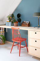 Spoke-back chair painted coral red at desk against blue wall